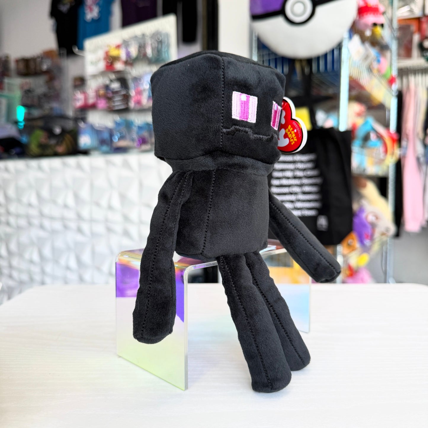 An Enderman plush from the video game Minecraft on a white table with a store in the background. 