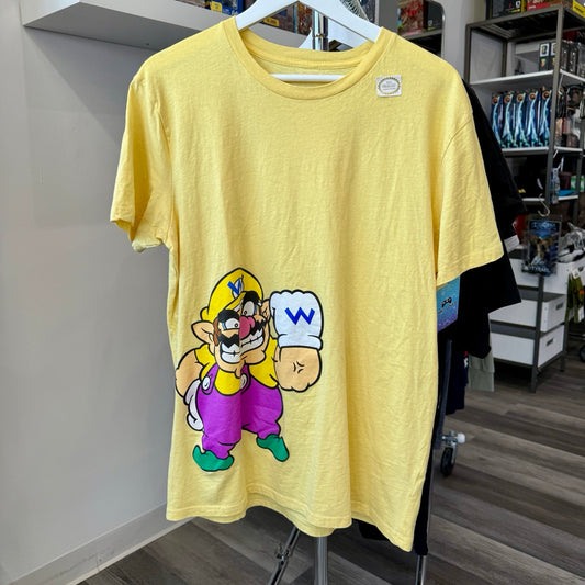 A yellow short-sleeve graphic T-shirt hanging on a white hanger, featuring a cartoon illustration of Wario. The shirt is displayed in a retail store setting.