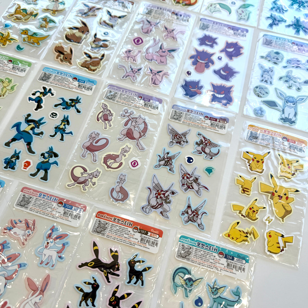 A collection of Pokémon-themed sticker sheets arranged in a grid on a white surface. The sheets feature various colorful Pokémon characters, including Eevee, Pikachu, Mew, and others, each in its own clear plastic packaging with Korean labels.