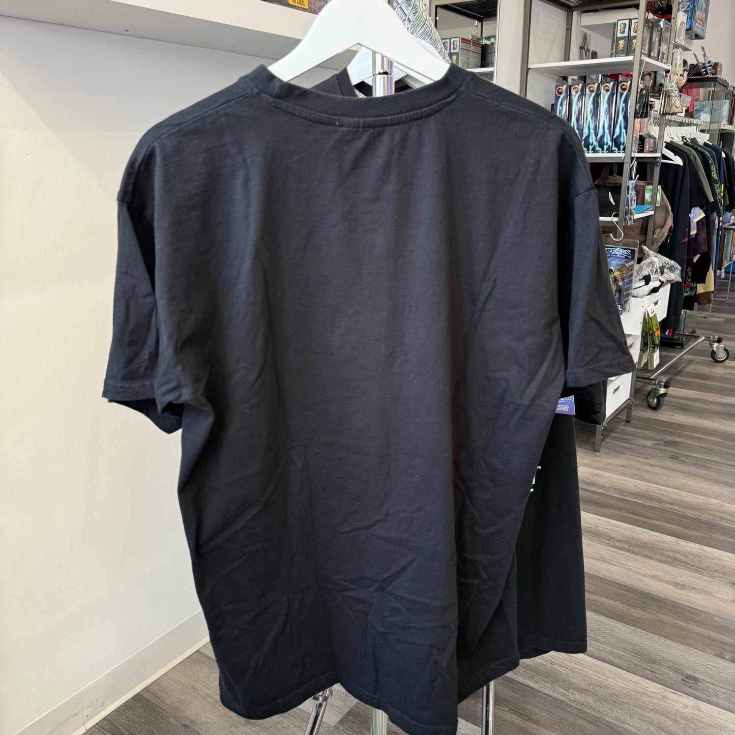 A plain black short-sleeve t-shirt hanging on a white hanger, showing the back view in a retail store setting.