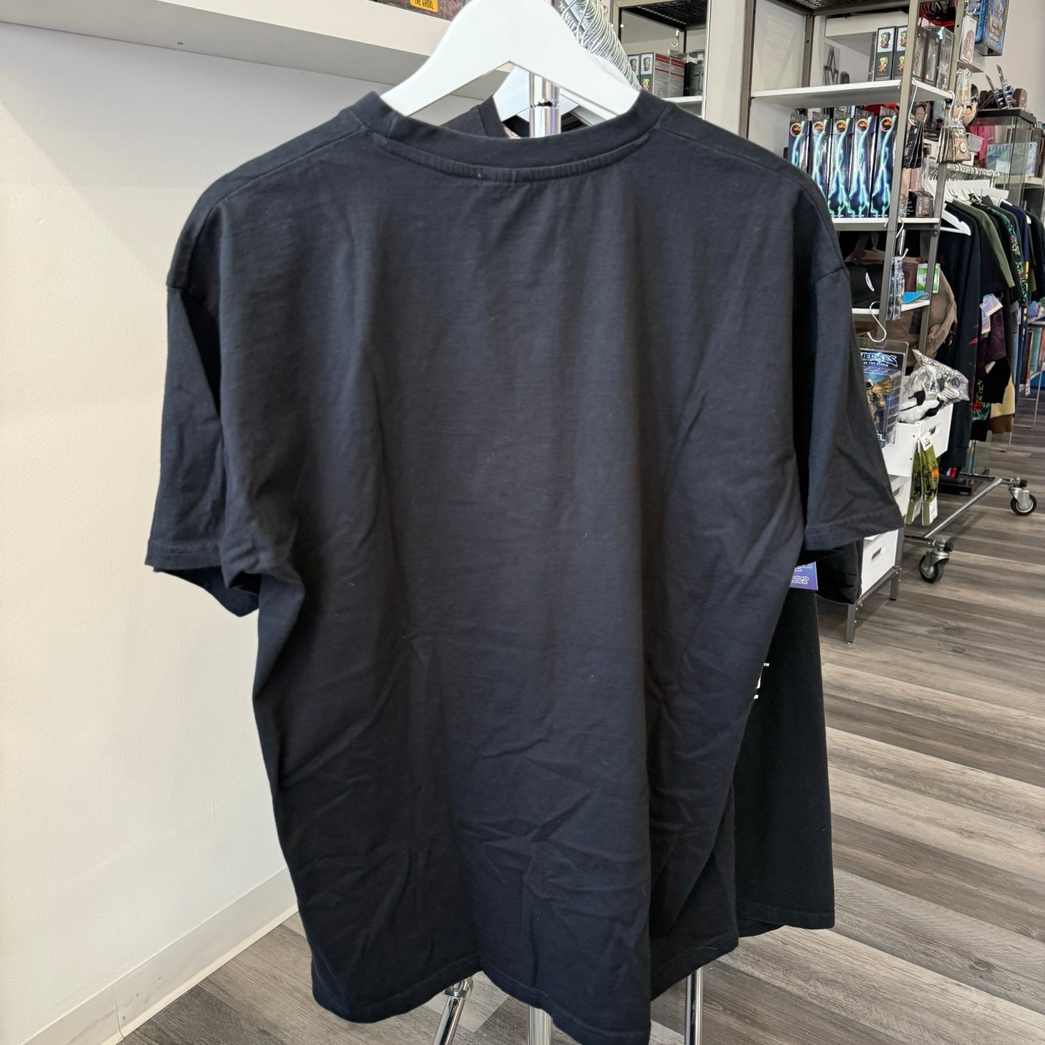 A plain black short-sleeve t-shirt hanging on a white hanger, showing the back view in a retail store setting.