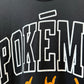 Close-up of a black T-shirt featuring large white outlined POKEMON lettering and orange graphic elements below.