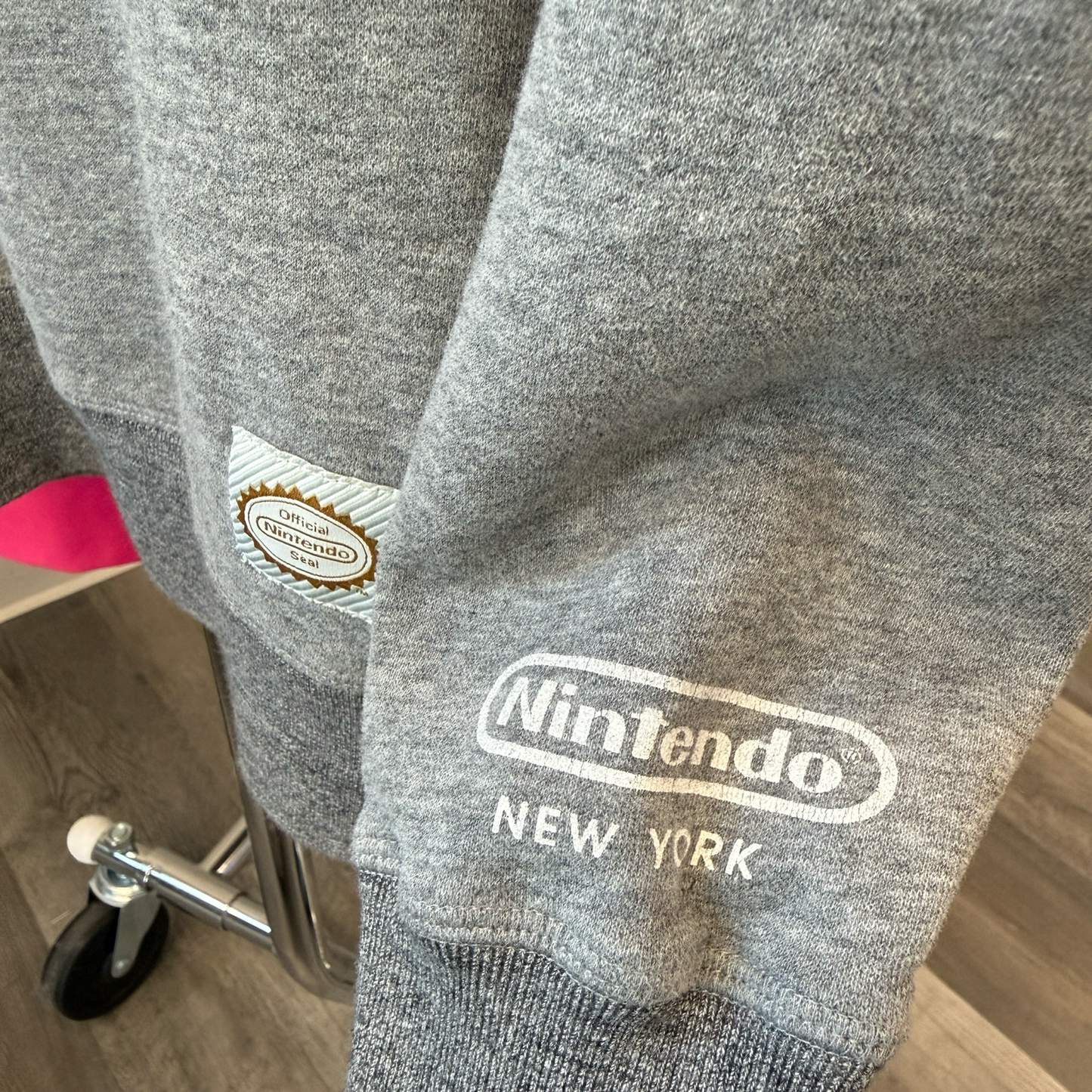 Upclose shot of grey sweatshirt with Official Nintendo Seal patch and Nintendo New York logo printed on sleeve. 
