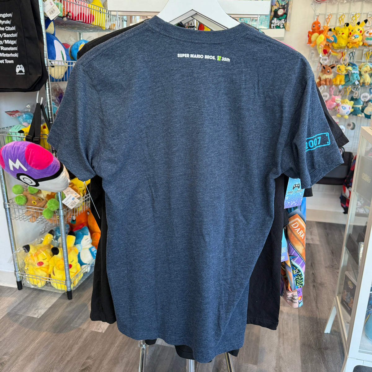 A heathered slate blue t-shirt is shown from the back, hanging on a white hanger in a retail store. 