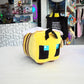 A bee plush from the video game Minecraft on a white table with a store in the background. 