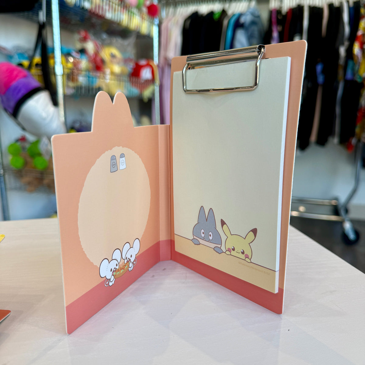An orange and red Pokémon themed memo pad clipboard with a store in the background. 