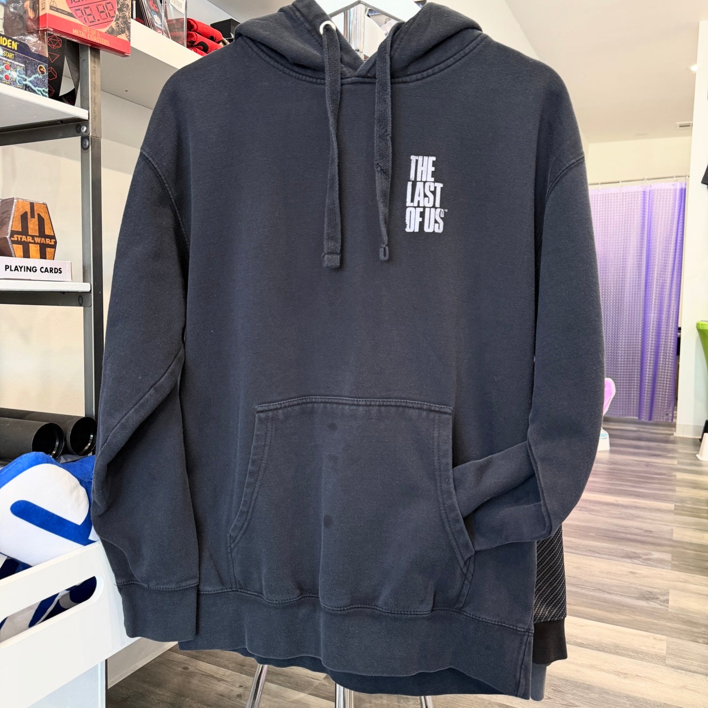 Black hoodie with 'The Last of Us' logo on a rack in a store.