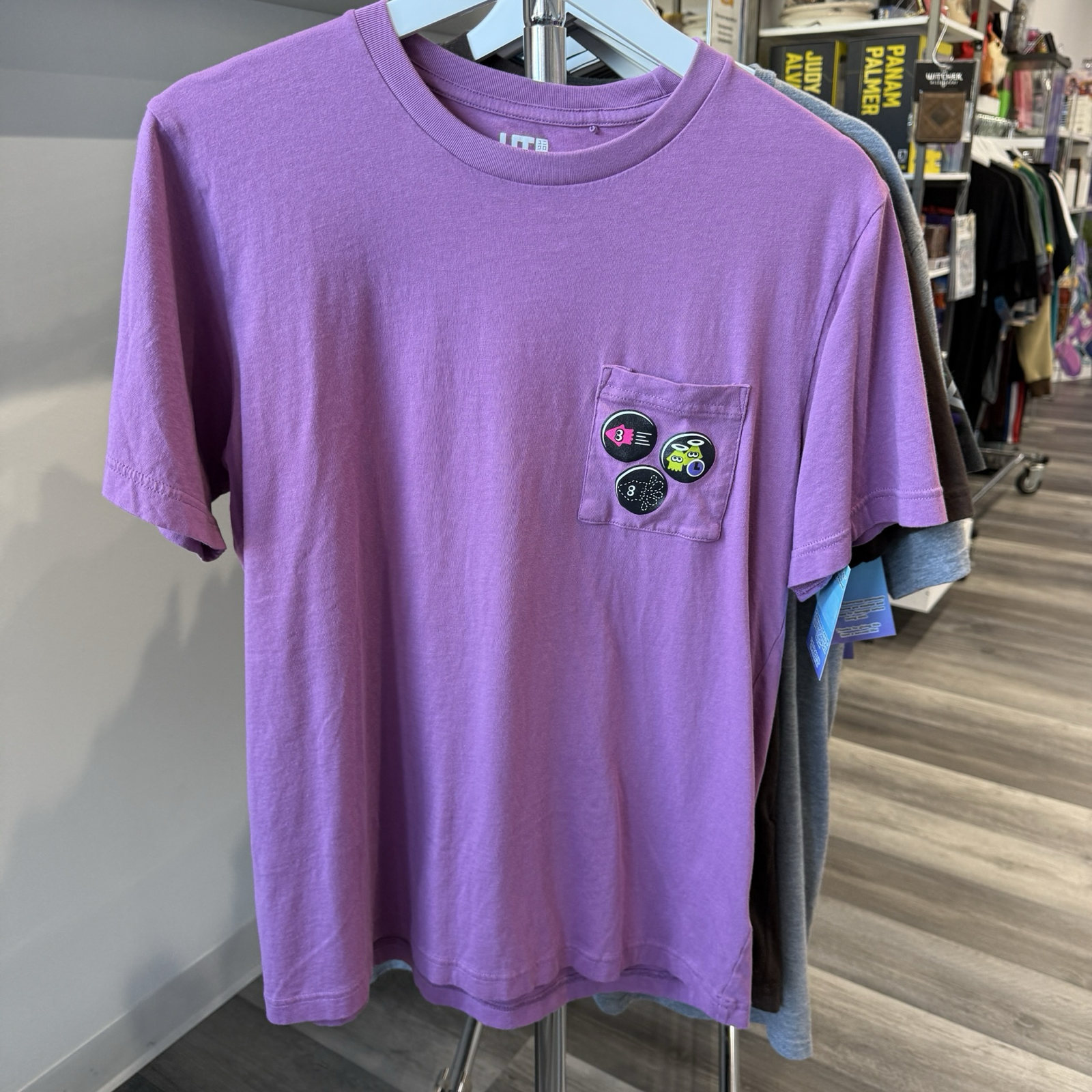 Purple shirt with pocket. On the pocket are three circular graphics of squids from the video game, Splatoon. 