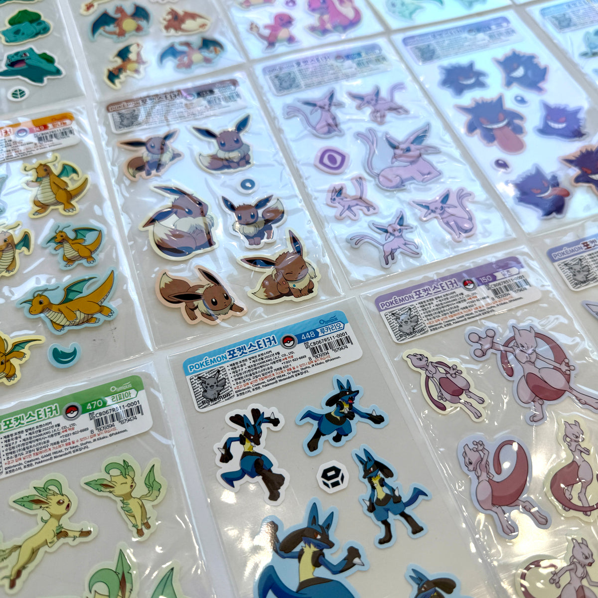 A collection of Pokémon-themed sticker sheets arranged in a grid on a white surface. The sheets feature various colorful Pokémon characters, including Eevee, Pikachu, Mew, and others, each in its own clear plastic packaging with Korean labels.