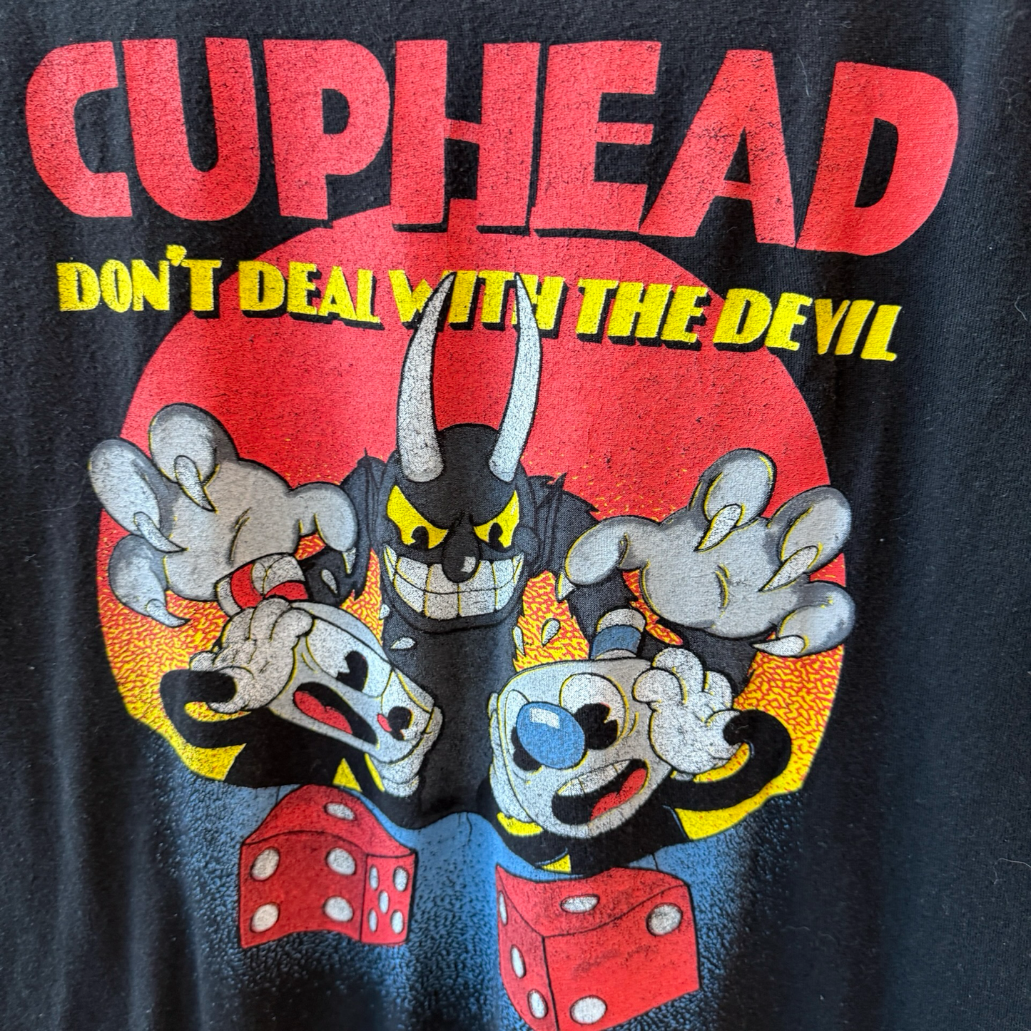 Close up shot of black tshirt with Cuphead Deal with the Devil graphic in red, yellow, and black. 