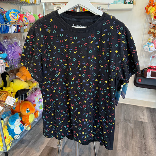 A black short-sleeve t-shirt with a colorful all-over pattern of PlayStation controller-style symbols (circles, squares, triangles, crosses) hanging on a white hanger in a retail store.