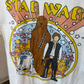 Close up shot of white tshirt with 1960s inspired graphic of R2D2, Chewbacca, and Han Solo from Star Wars. 