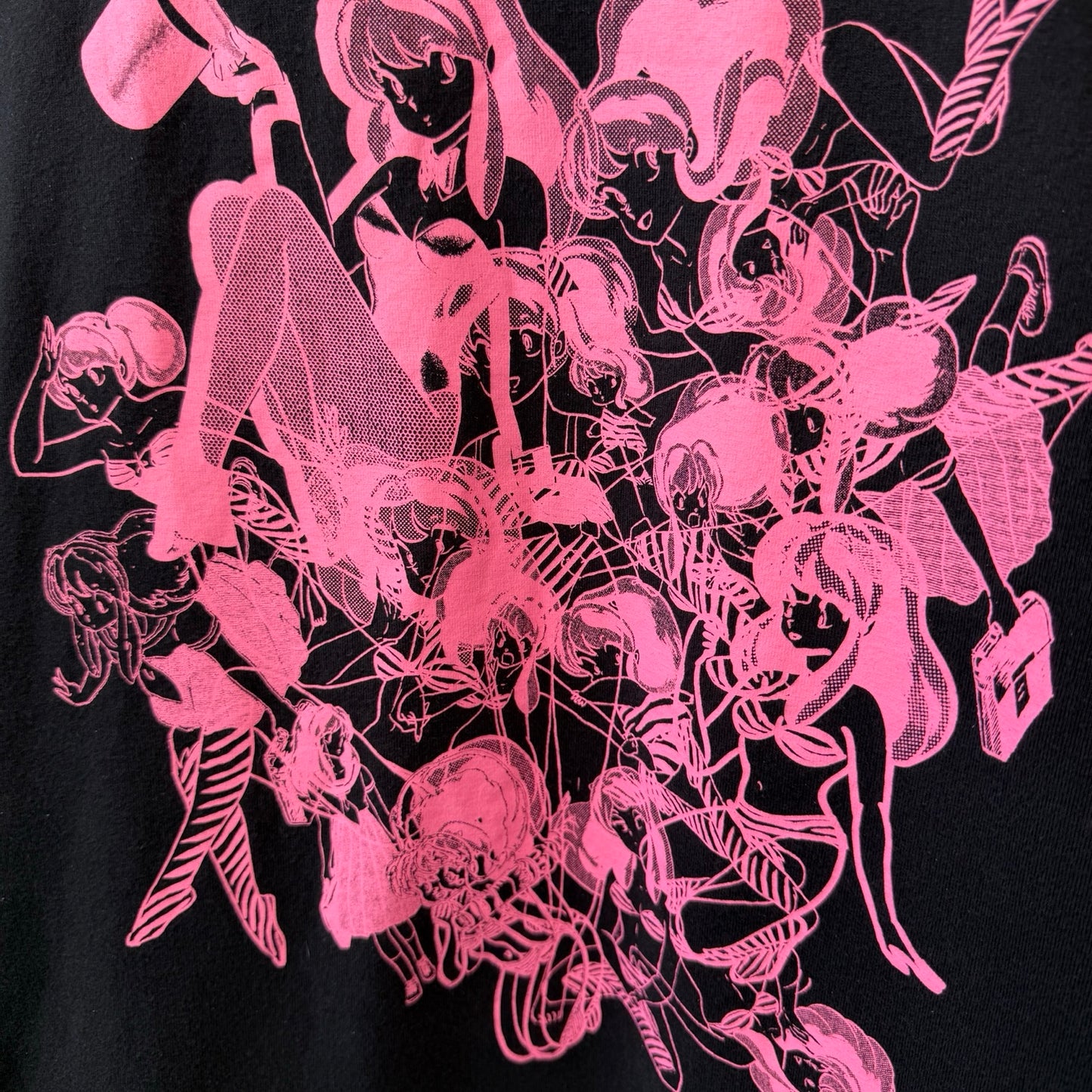 A close-up of a black garment featuring a vibrant hot pink graphic print of artwork of anime character Urusei Yatsura in a dense, overlapping collage.
