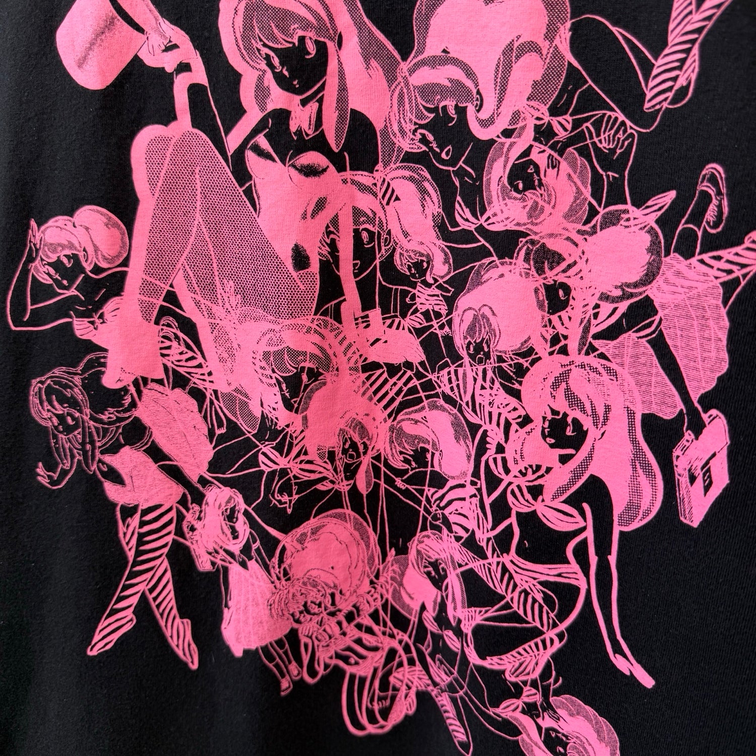 A close-up of a black garment featuring a vibrant hot pink graphic print of artwork of anime character Urusei Yatsura in a dense, overlapping collage.