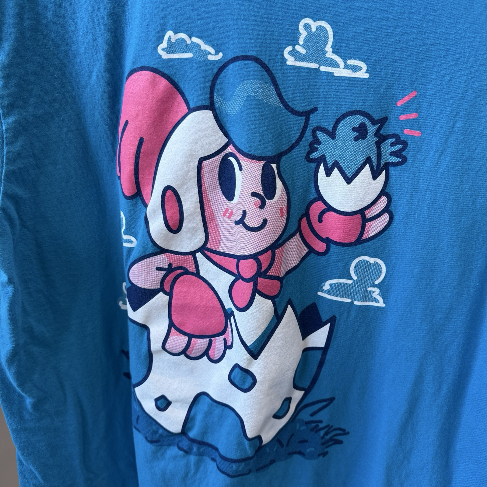 Close up shot of teal blue color tshirt with white and red graphic of boy sitting in a egg from video game, Billy Hatcher and the Giant Egg. 