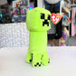 A  Creeper plush from the video game Minecraft on a white table with a store in the background. 