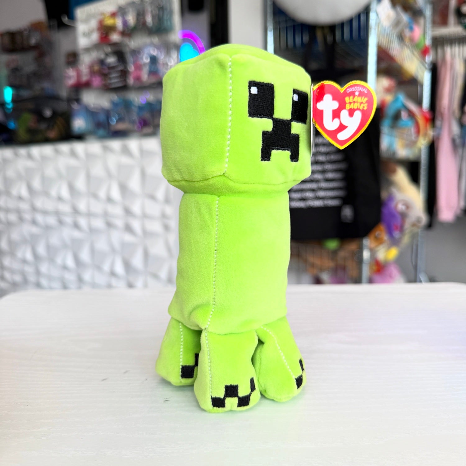 A  Creeper plush from the video game Minecraft on a white table with a store in the background. 