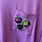 Up close view of purple shirt with pocket. On the pocket are three circular graphics of squids from the video game, Splatoon. 
