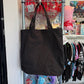 Black canvas tote bag hanging on a metal shelf in a store setting.