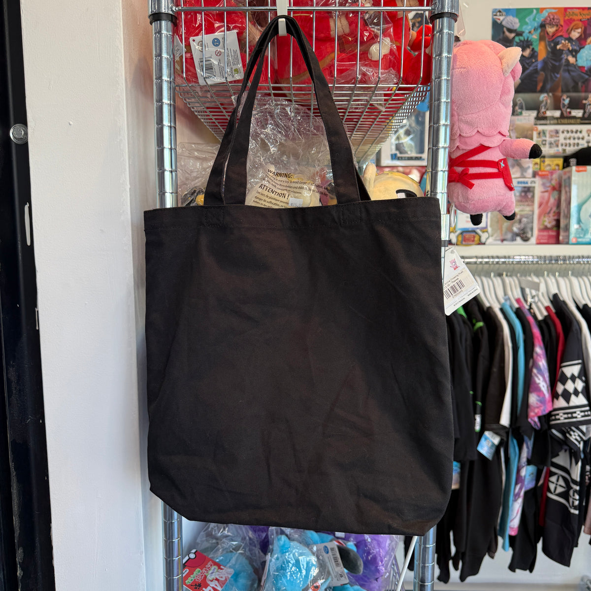 Black canvas tote bag hanging on a metal shelf in a store setting.