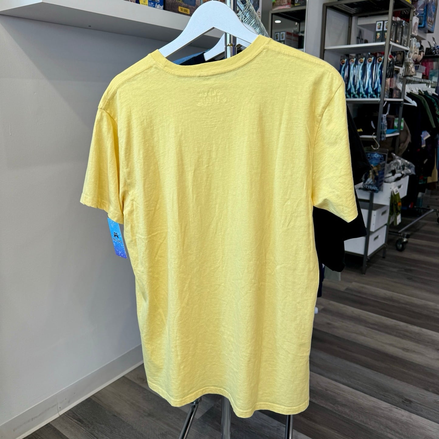 A light yellow short-sleeve crewneck t-shirt hanging on a white hanger on a clothing rack inside a retail store.