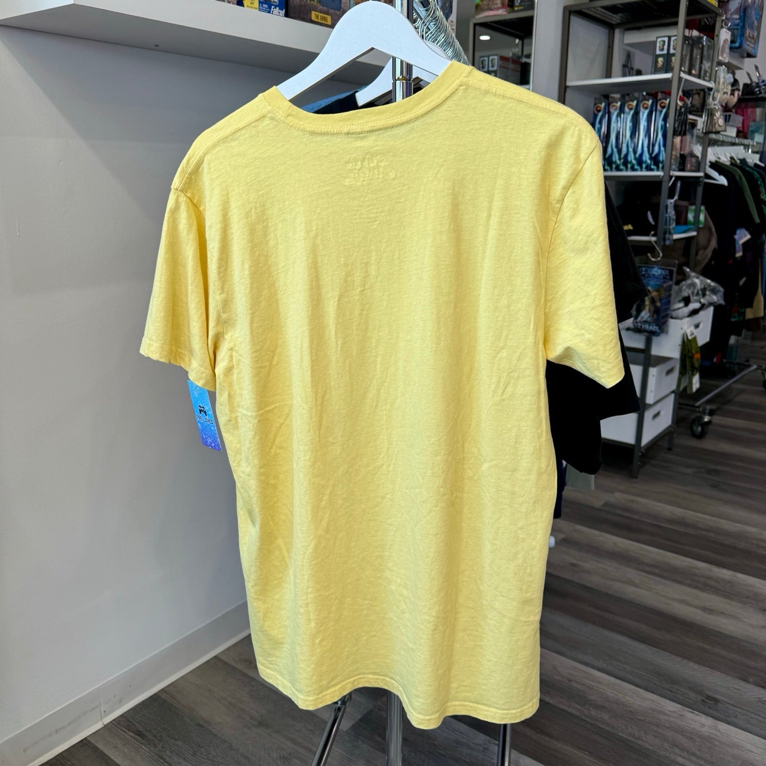 A light yellow short-sleeve crewneck t-shirt hanging on a white hanger on a clothing rack inside a retail store.
