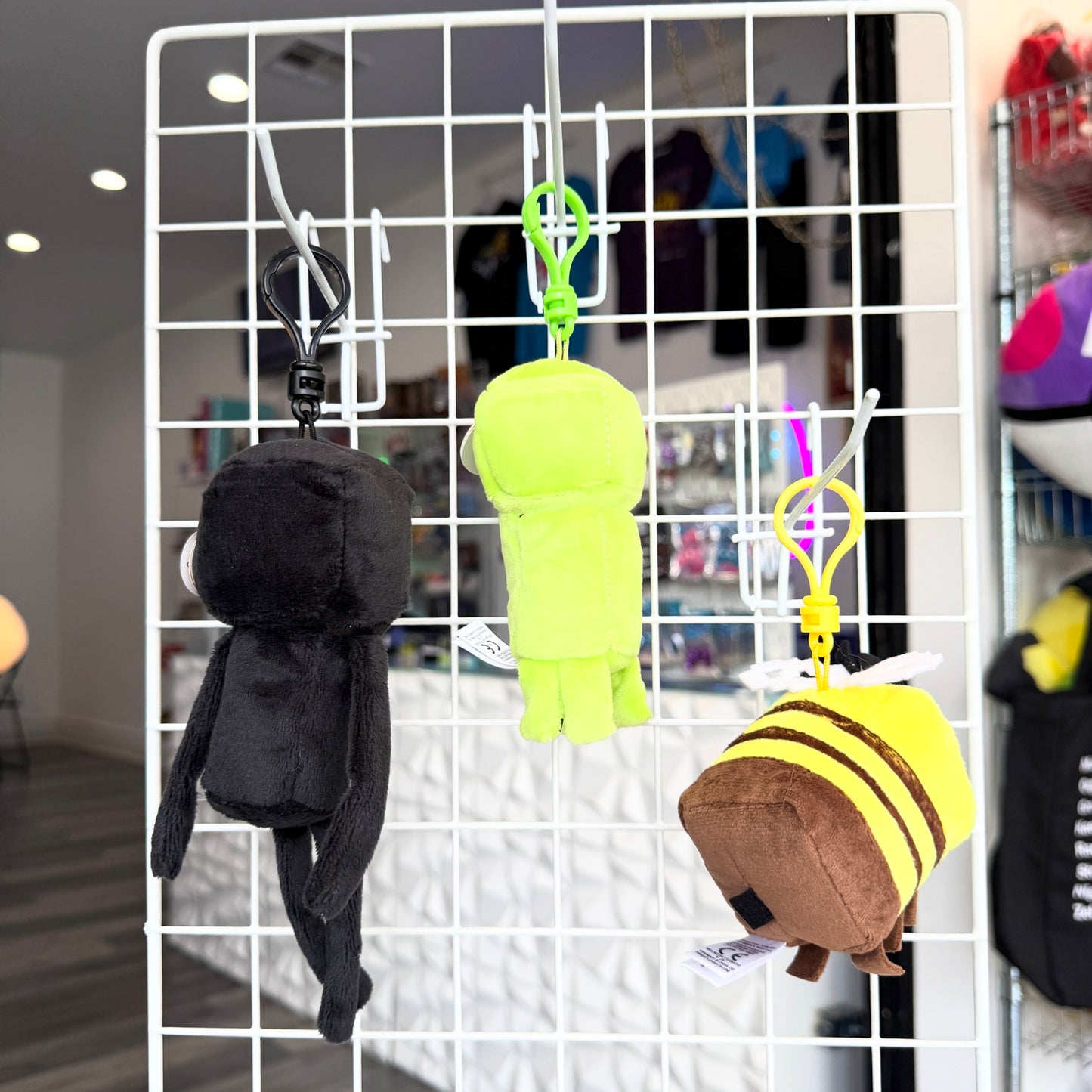 Three plush character keychains hanging from a white wire display grid in a retail store. 