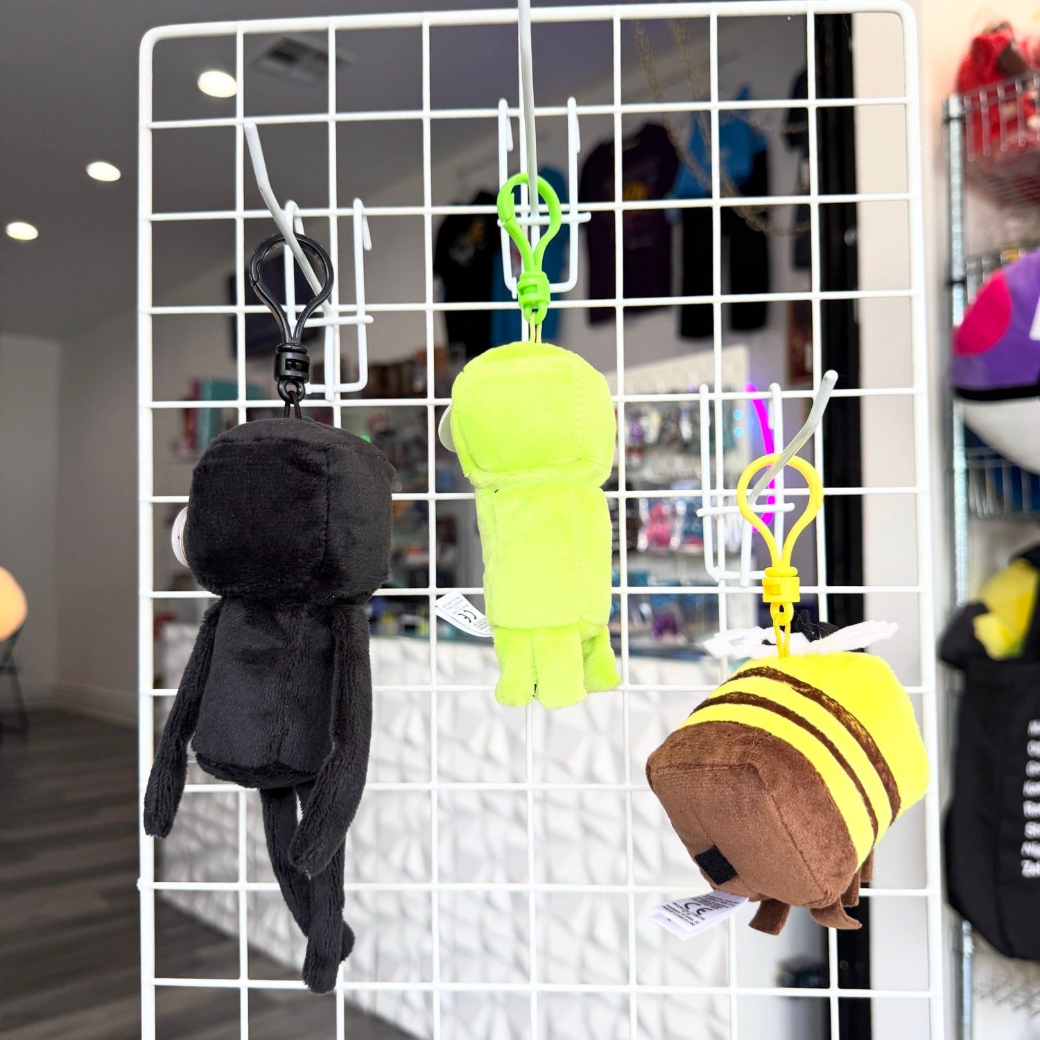 Three plush character keychains hanging from a white wire display grid in a retail store. 