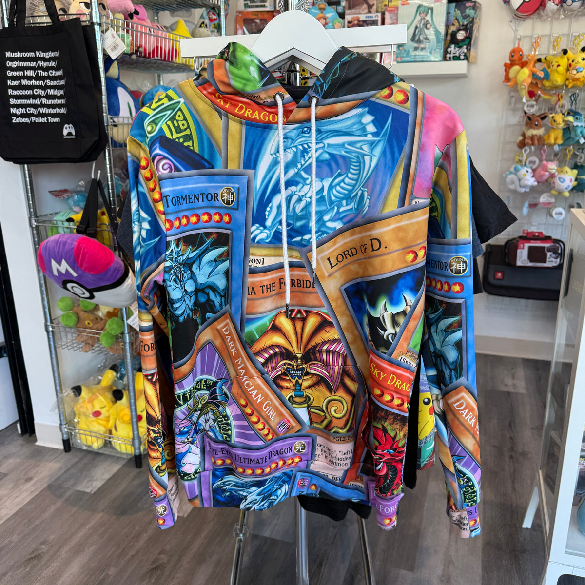 A colorful graphic hoodie featuring Yu-Gi-Oh! card art and character prints, hanging on a white hanger inside a retail store.