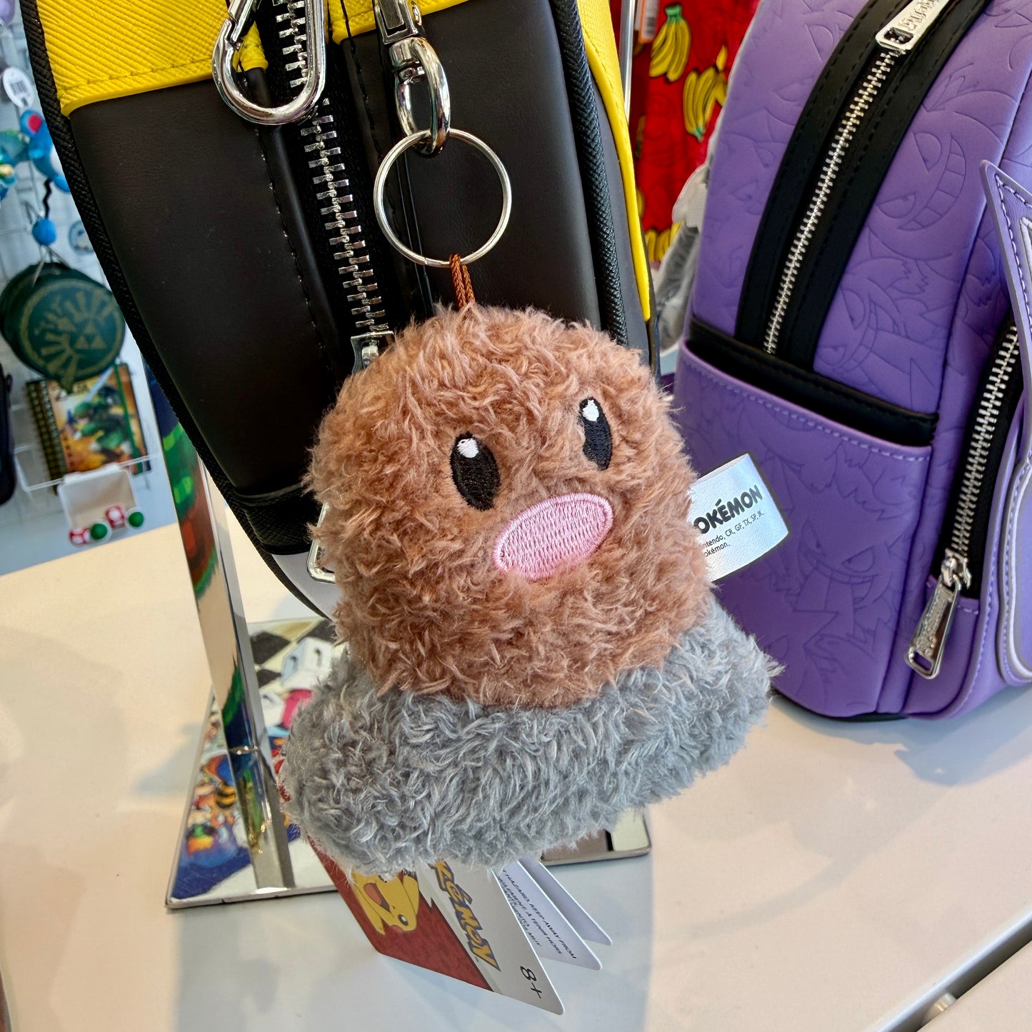 Fluffy, plush keychain of the Pokémon, Ditto hanging off a bag inside a store 