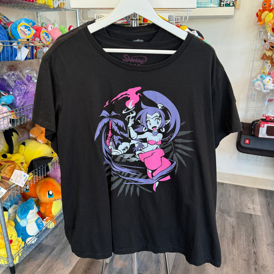 A black graphic t-shirt hanging on a white hanger in a retail store. The shirt features a colorful graphic from the video game, Shantae. 