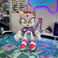 A plush toy of a purple cat character with yellow eyes, white gloves, and pink-and-white sneakers, displayed on a colorful gaming-themed surface in a retail setting.