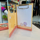 A yellow and red Pokémon themed memo pad clipboard with a store in the background. 