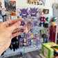 A hand holds a clear sheet of Pokémon Gengar stickers with a blurred image of a store in the background. 