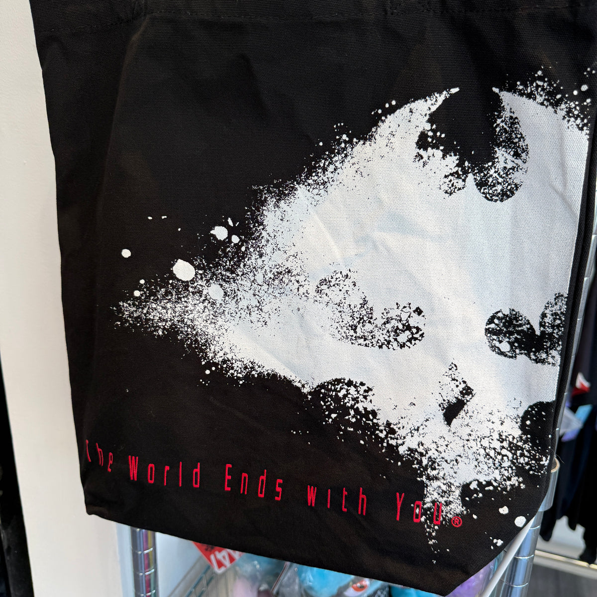 Close up of a black canvas tote bag with graphic from the video game, The World Ends With you on the front. 