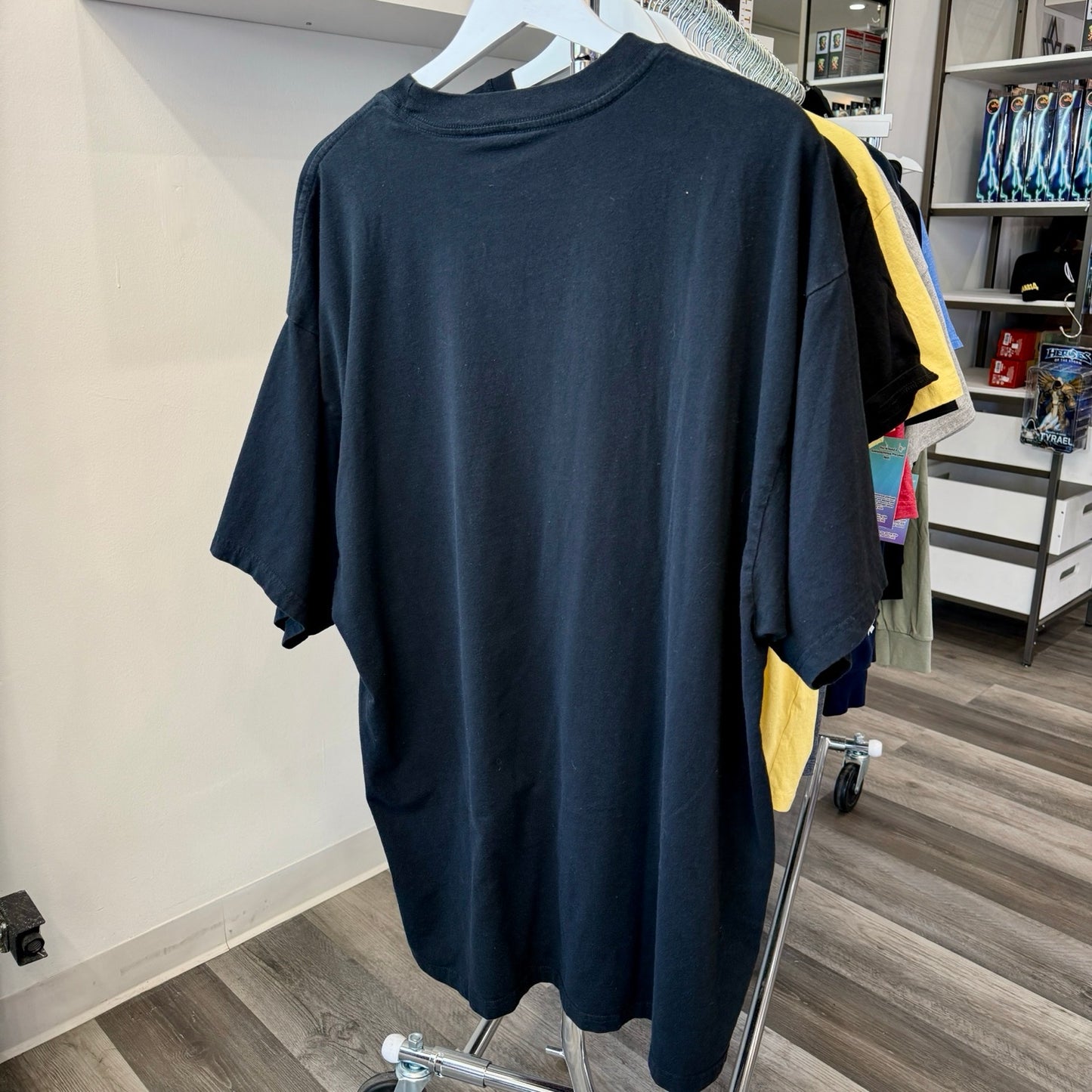 A large black oversized t-shirt hanging on a white hanger on a clothing rack inside a retail store.
