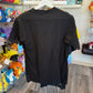 A black short-sleeve t-shirt is shown from the back, hanging on a white hanger in a retail store.