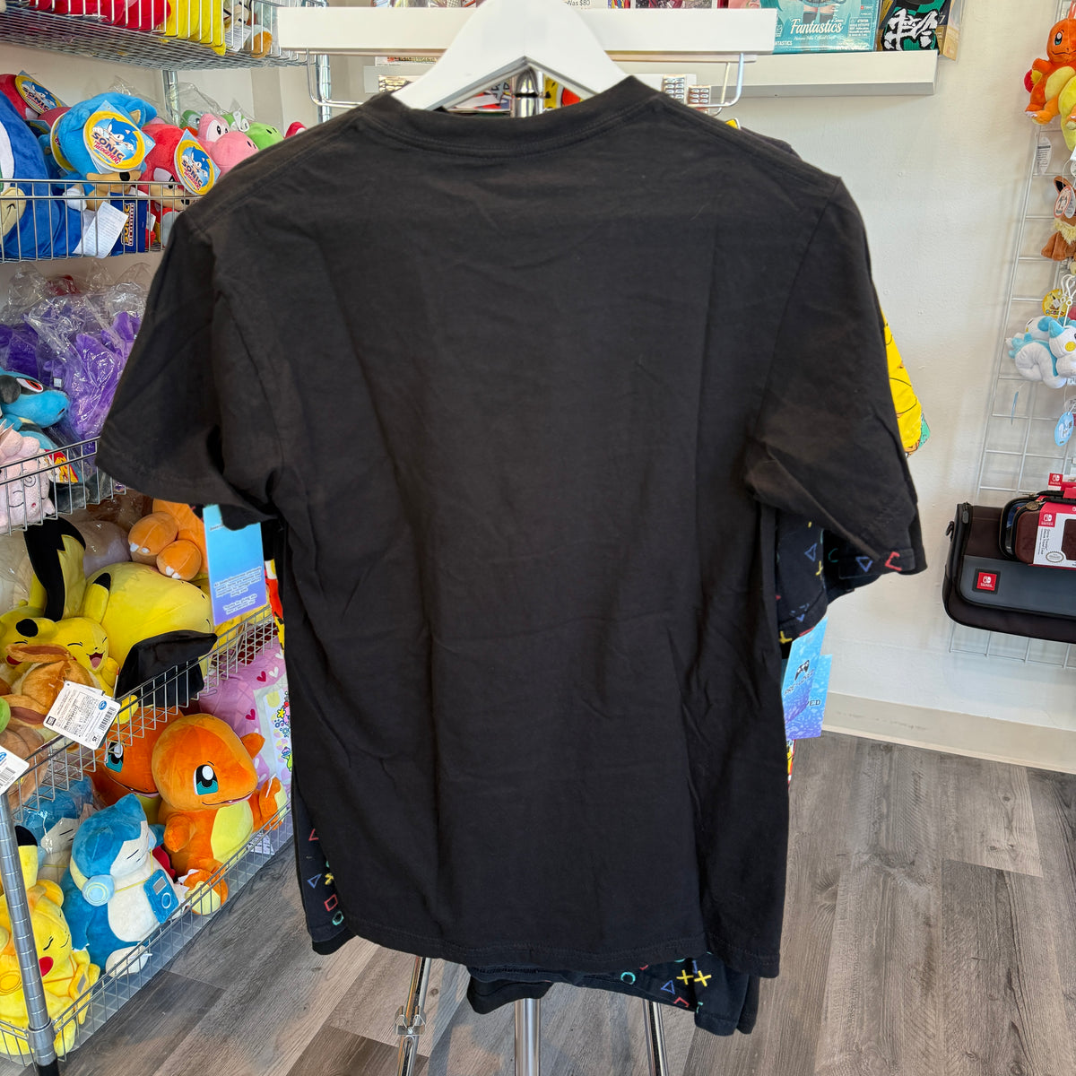 A black short-sleeve t-shirt is shown from the back, hanging on a white hanger in a retail store.