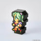 A pixel-art collectible figure made of black block-like pieces, featuring a green-haired character with colorful clothing details, photographed on a clean light gray background. A small SQUARE ENIX copyright mark appears in the bottom right corner.