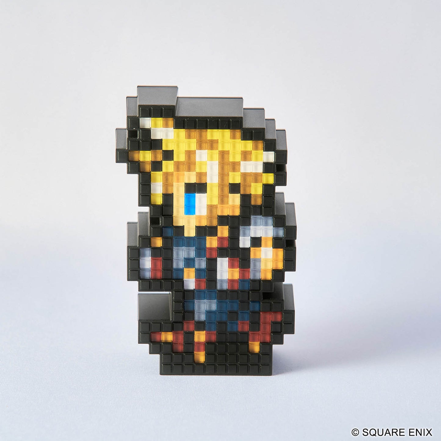 A pixel-art collectible figurine of a fantasy character made from black, gray, yellow, blue, white, and orange blocks, standing on a light gray background. A copyright notice for SQUARE ENIX is visible in the bottom right corner.