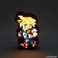 A pixel-art character lamp glowing against a dark gray background. The character has yellow hair, a blue top, and red/orange accents, with a black silhouette.