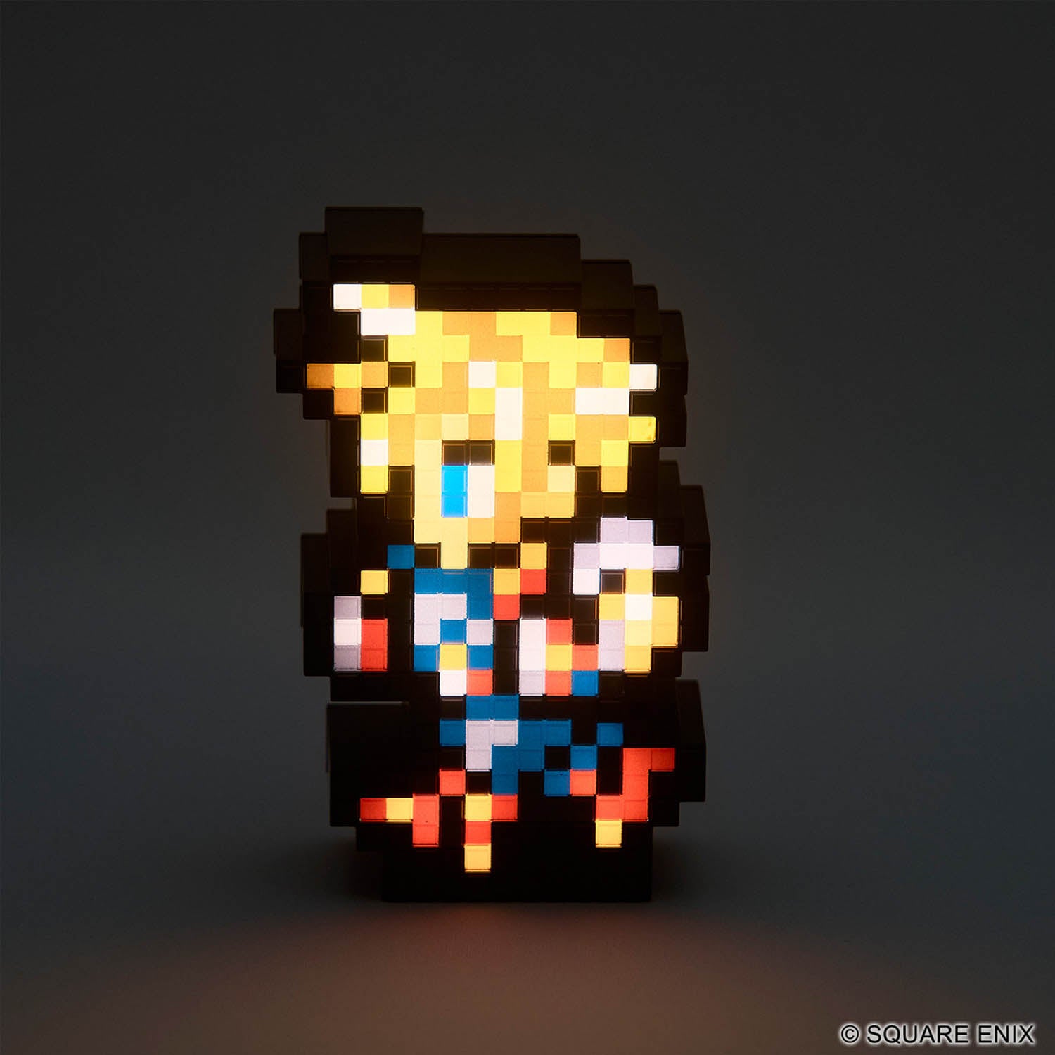 A pixel-art character lamp glowing against a dark gray background. The character has yellow hair, a blue top, and red/orange accents, with a black silhouette.