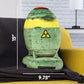 Nuke shaped plush toy on a black blanket laid across a yellow sofa. Living room in the background. White text and lines show measurements of 15 by 9.75 inches.