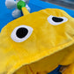 close up up a yellow Pikmin plush character hat with big eyes and white flower topper. 