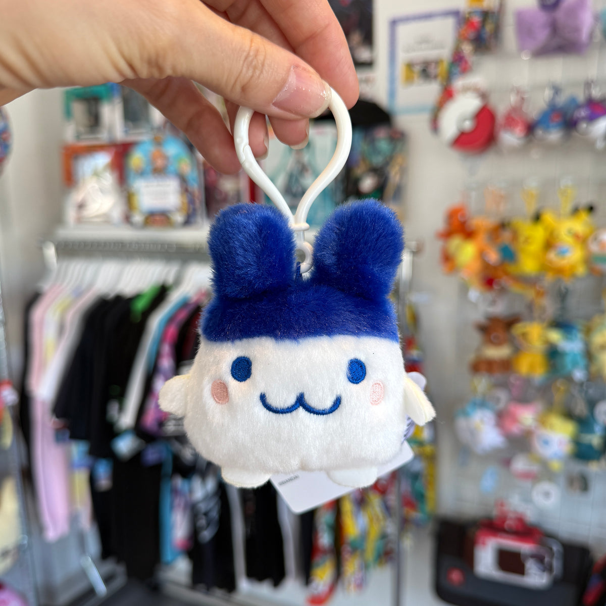 Hand holding white and blue Tamagotchi character with a store in the background. 