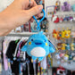 Hand holding blue dolphin Tamagotchi character with a store in the background. 