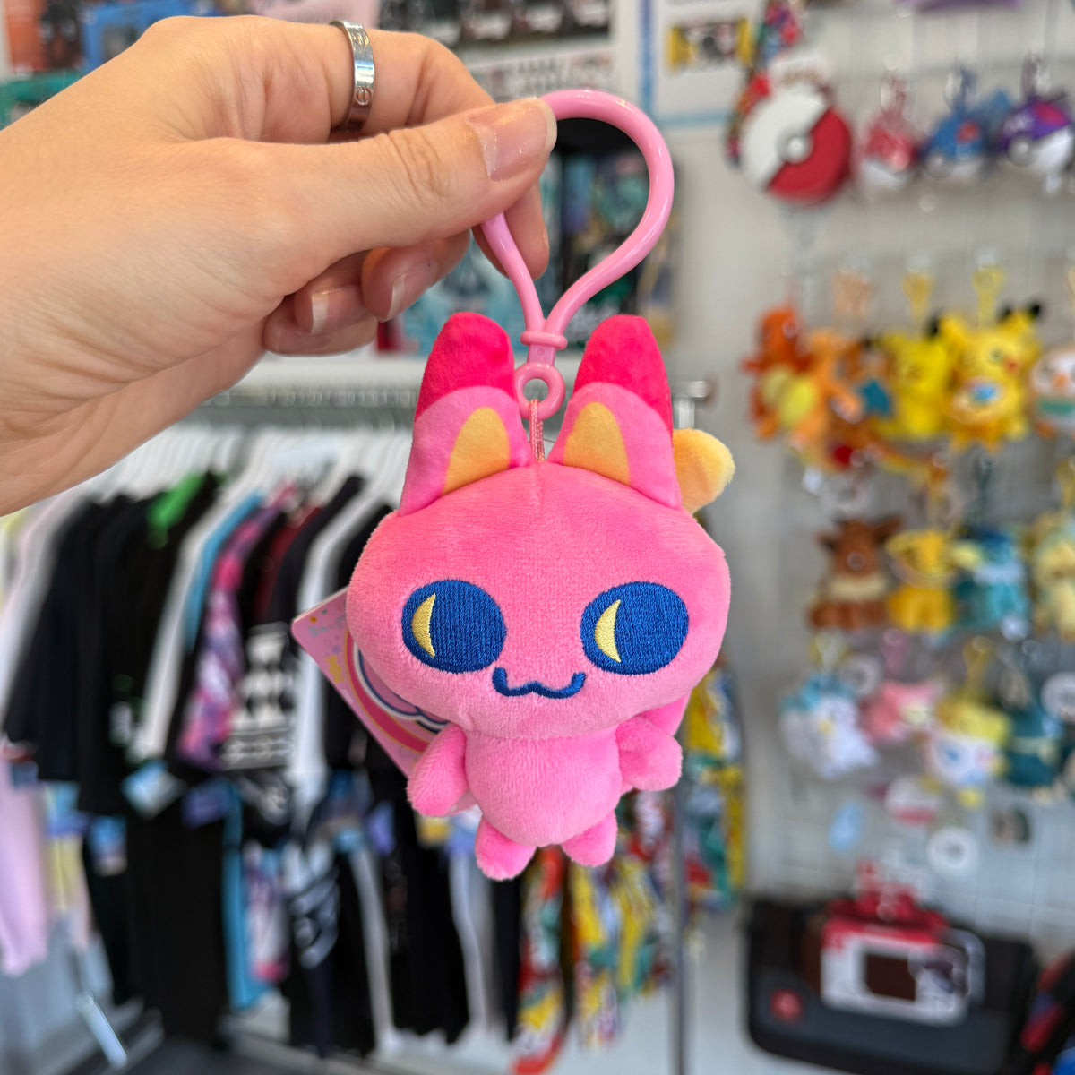Hand holding pink cat Tamagotchi character with a store in the background. 