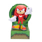 A Knuckles collectible figurine from Sonic the Hedgehog standing on a green textured base with a circular green backdrop. Knuckles is depicted with his signature red body, white gloves, yellow and orange sneakers, and green socks, set against a plain white background.