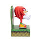 A Knuckles figurine standing on a green platform with a circular green backdrop, shown against a plain white background.