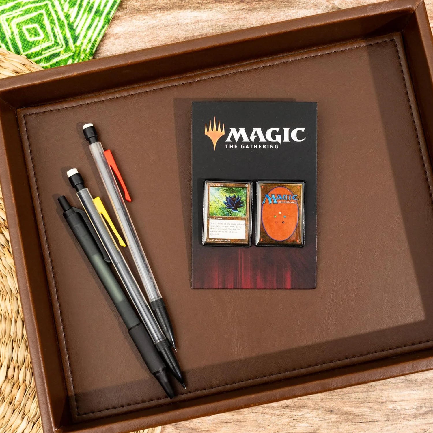 Brown leather desk tray holding pens and mechanical pencils and Magic the Gathering pins 